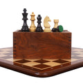 Championship ebonised boxwood chess pieces standing on top of a wooden storage box on a matching board.