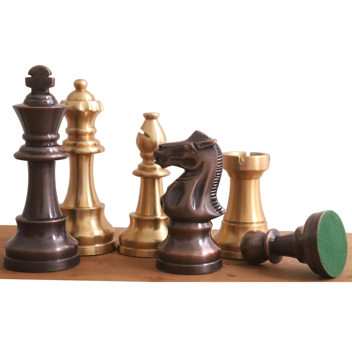 Antiqued copper and brass Pro Staunton chess pieces with a fallen pawn revealing a green felt base.