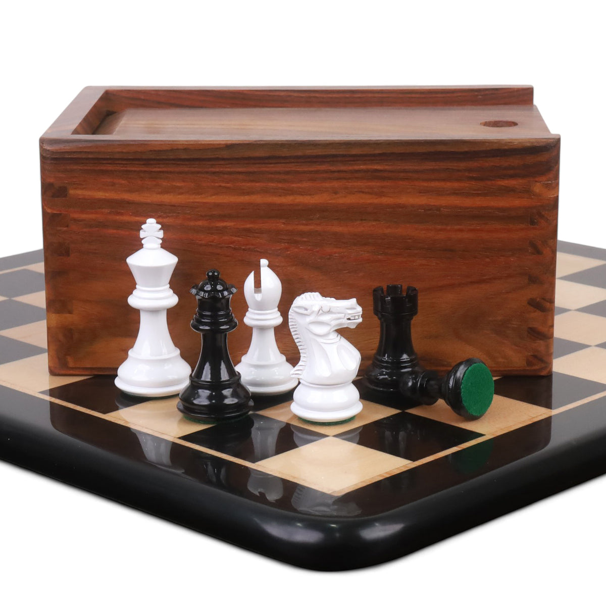 White and black Pro Staunton chess pieces standing in front of a golden rosewood storage box on an ebony board.