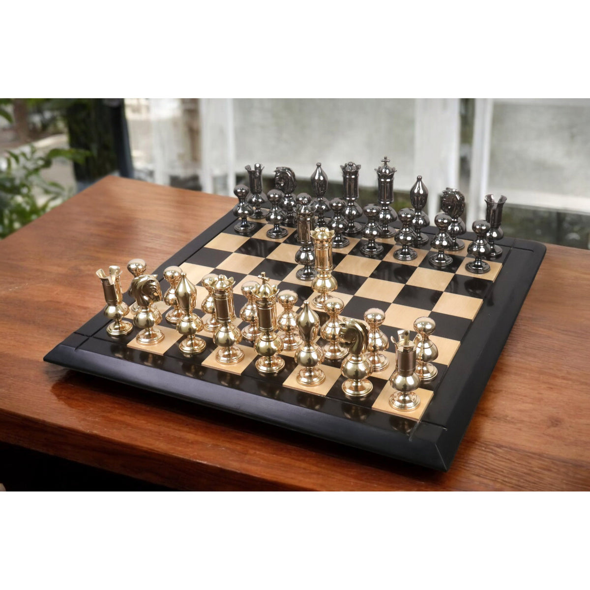 Full Victorian series brass metal luxury chess set with metallic gold and grey pieces set up on a chessboard.