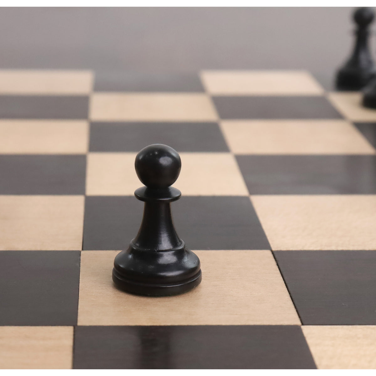 Ebonised boxwood pawn from the 2.4 inch Pro Staunton set on a wooden chess board.