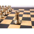 Mirror-polished gold brass rook chess piece isolated on a wooden chessboard square.