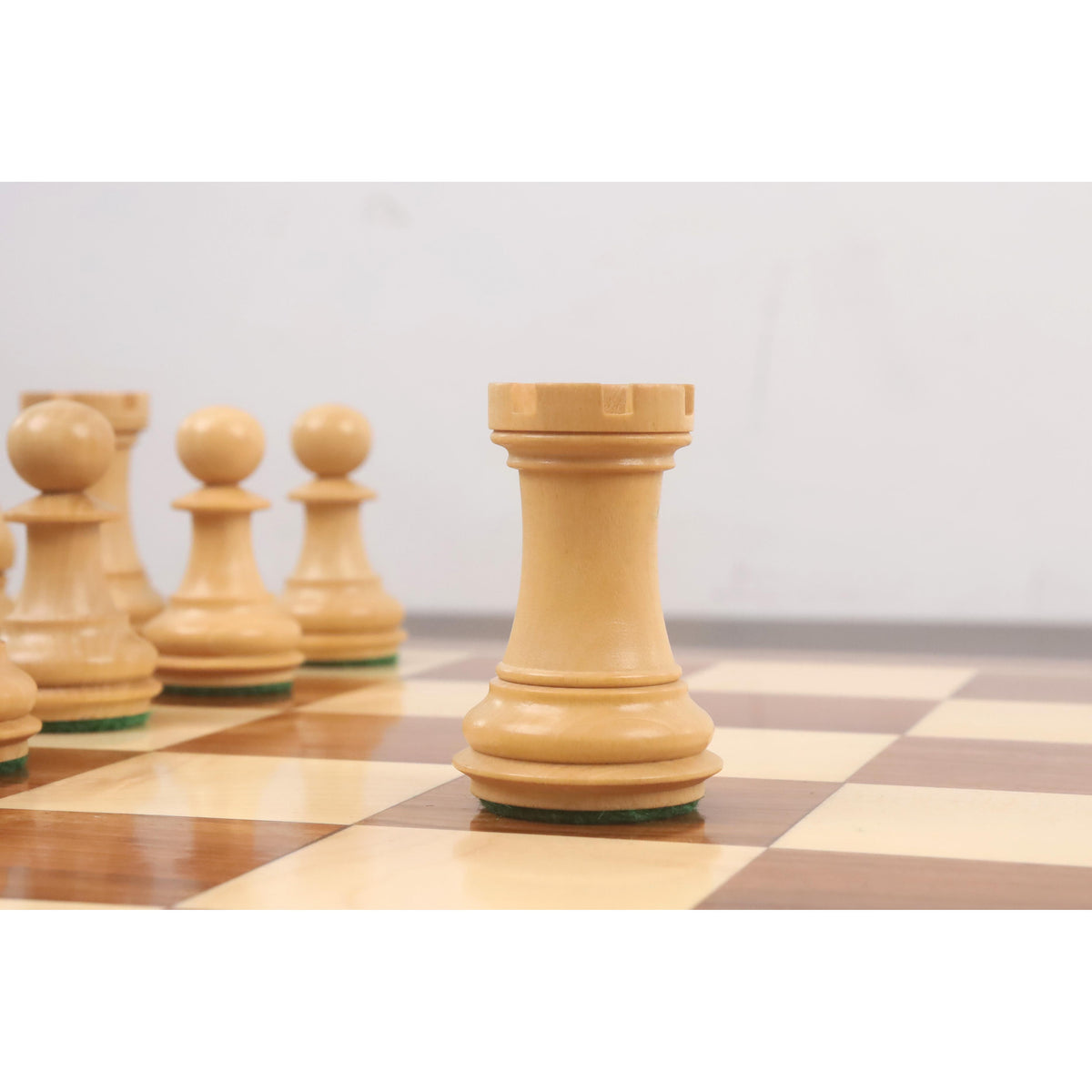 Boxwood Staunton rook with a weighted chamfered base standing on a wooden chessboard.