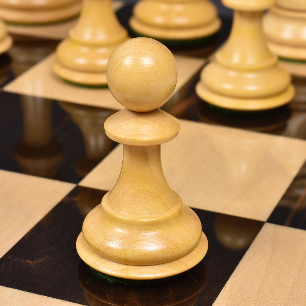 Detailed view of a boxwood pawn from the luxury Sleek Staunton chess set resting on a glossy dark square.