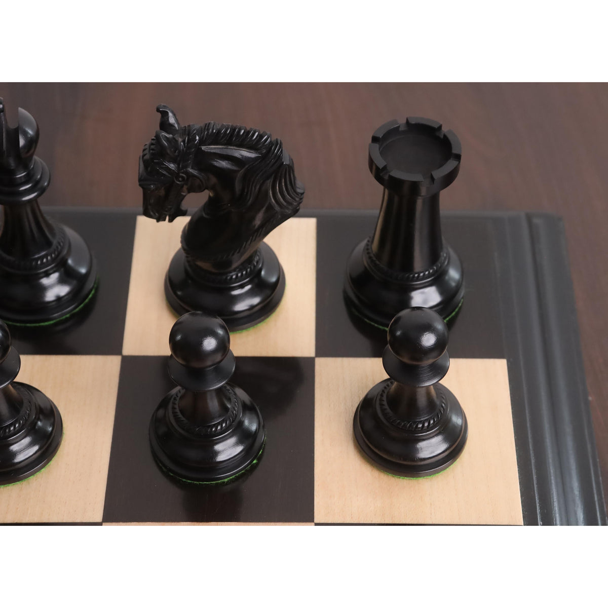 Jet-black ebony wood pawns, knight, and rook on a luxury wood chessboard corner.