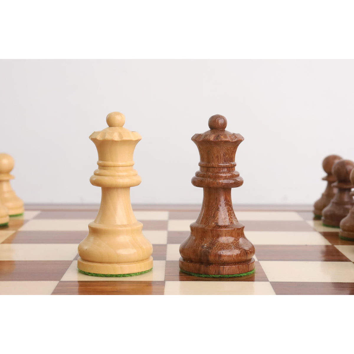 Carved boxwood and golden rosewood queens from the Staunton tournament set standing on a board.