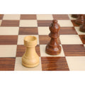 Boxwood rook and golden rosewood bishop pieces from the tournament set displayed on a wooden board.