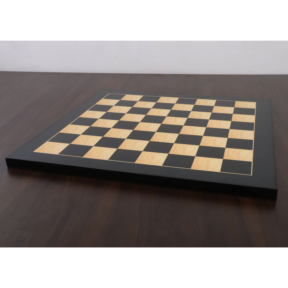 Angled view of a 17 inch ebony and maple wood printed chess board with 45mm squares on a dark table.