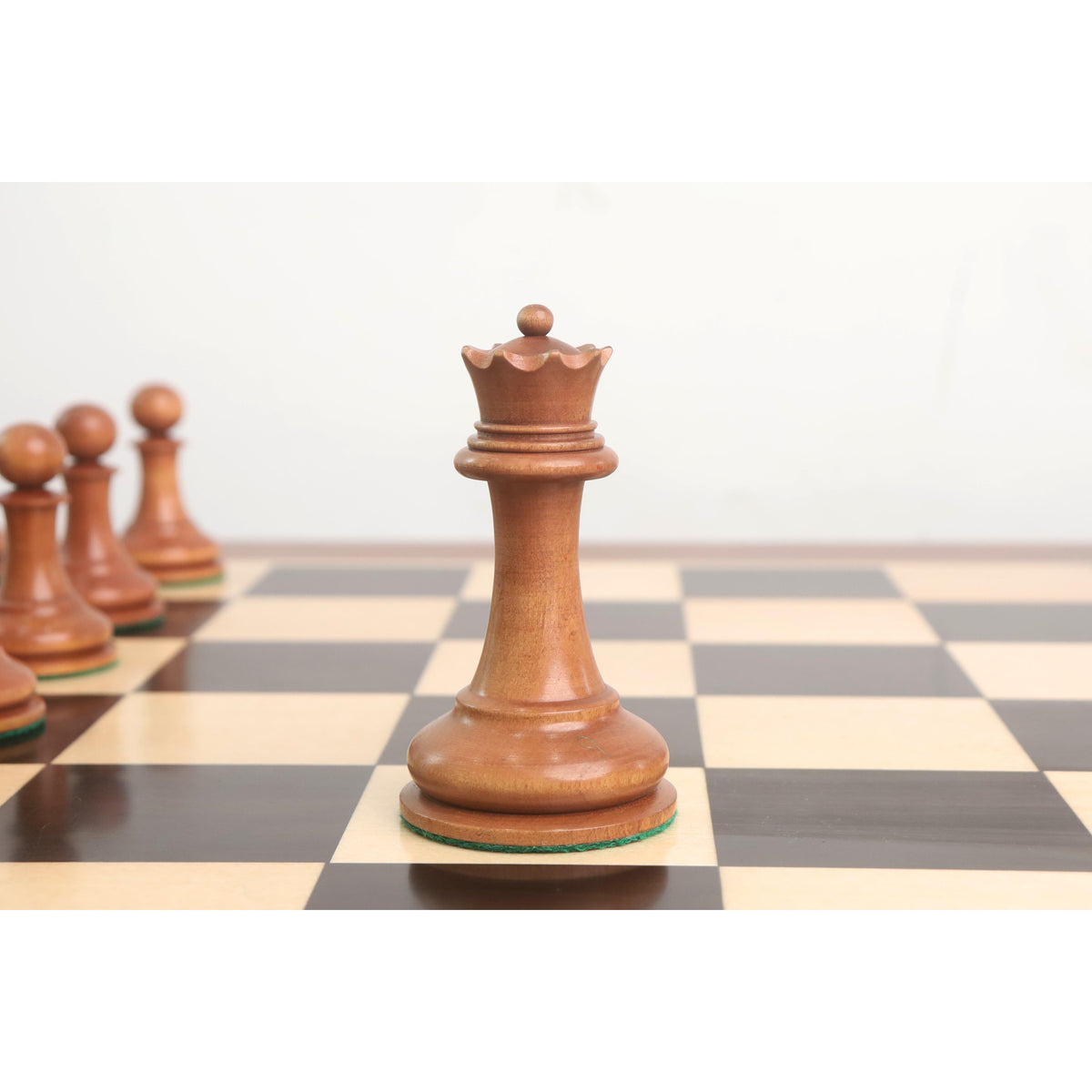Antiqued boxwood queen piece from the 1849 Cooke Staunton series on a dark and light wood board.