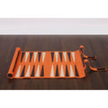 Handcrafted roll-up backgammon board in orange finish displayed on a dark table.
