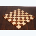 Square borderless chess board in golden rosewood and maple resting on a dark wood table.