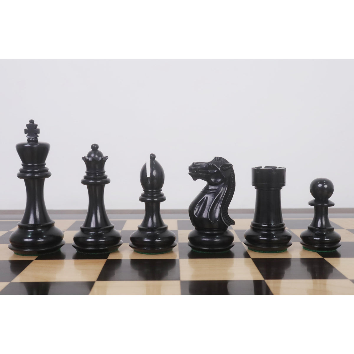Close-up profile of Ebonised Pro Staunton pieces lined up on a wooden chessboard.