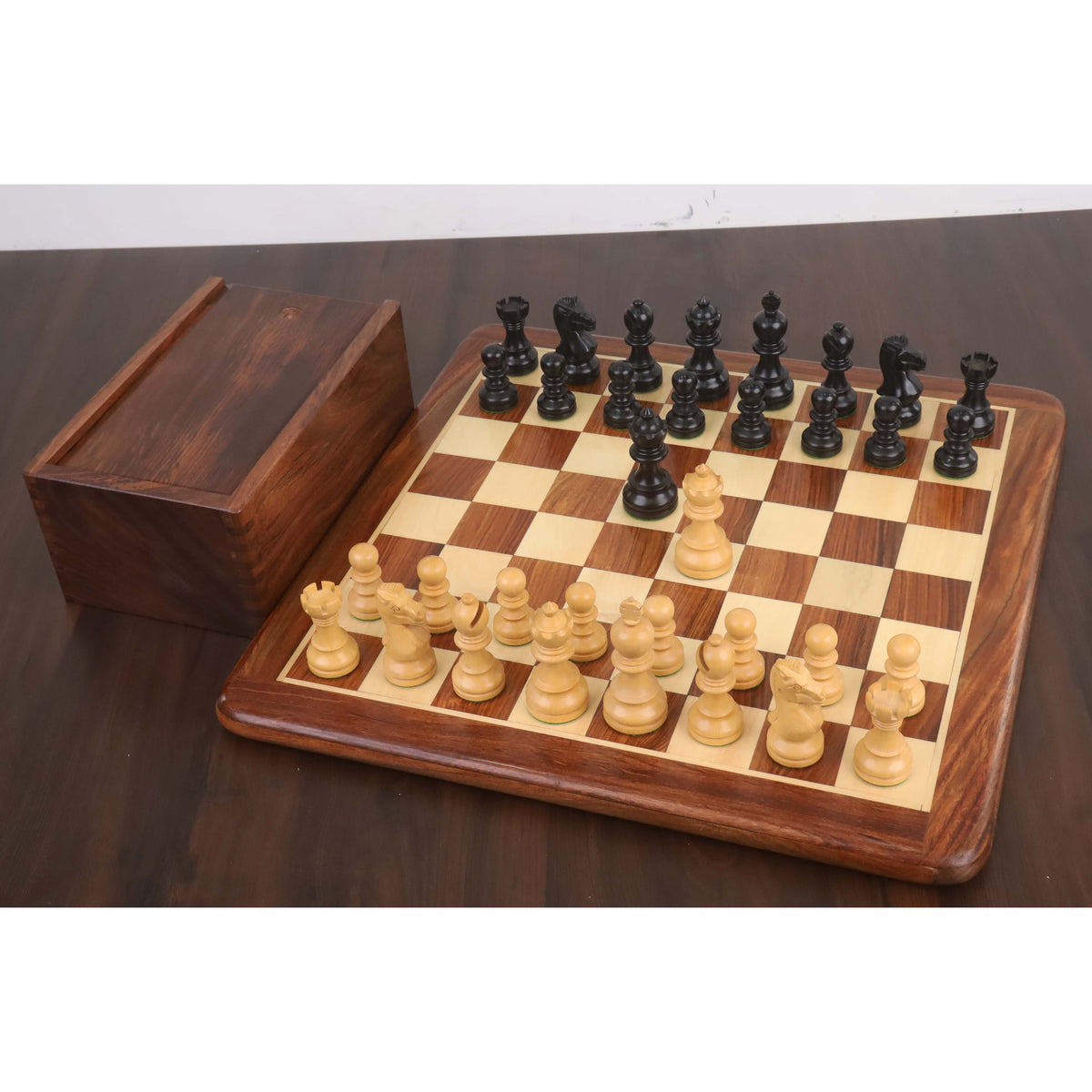 Full set of Taj Mahal ebonised boxwood chess pieces arranged on a wooden board beside a storage box.