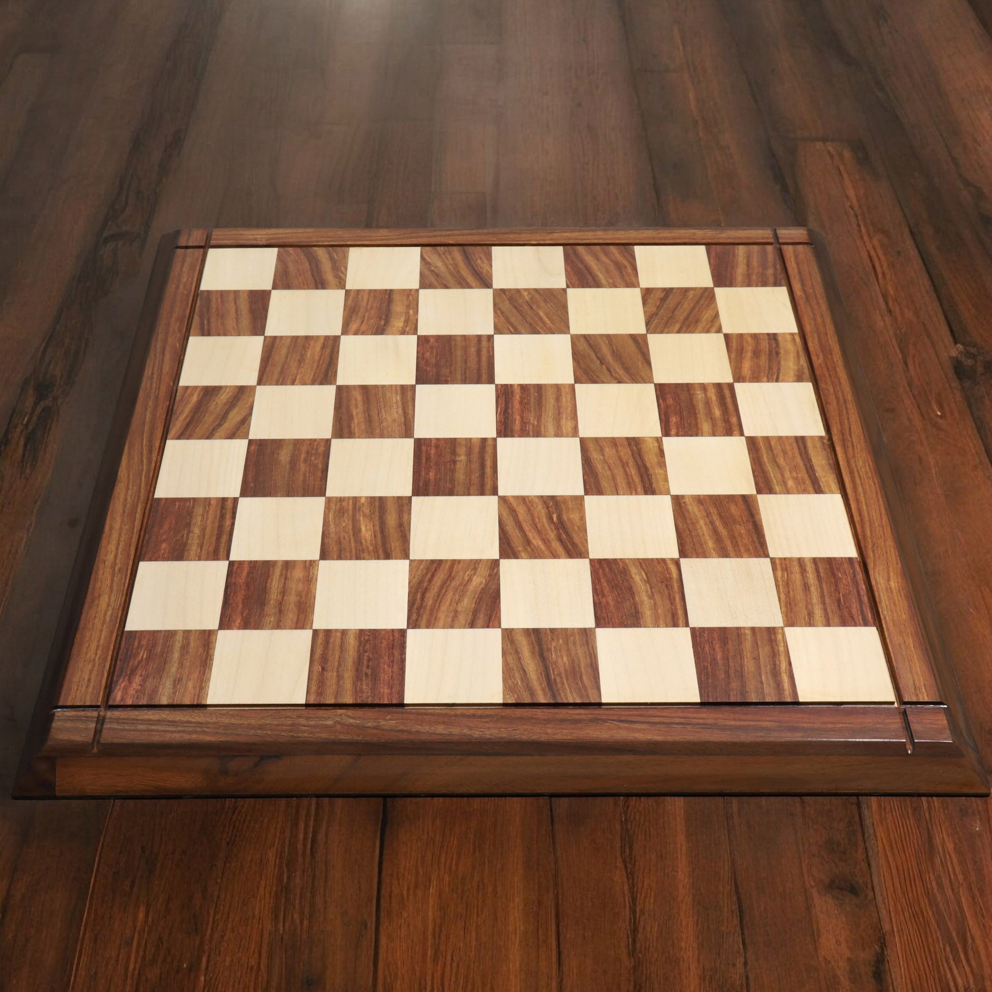 Top-down lifestyle view of a 21 inch solid golden rosewood and maple wood chess board on a wooden floor.