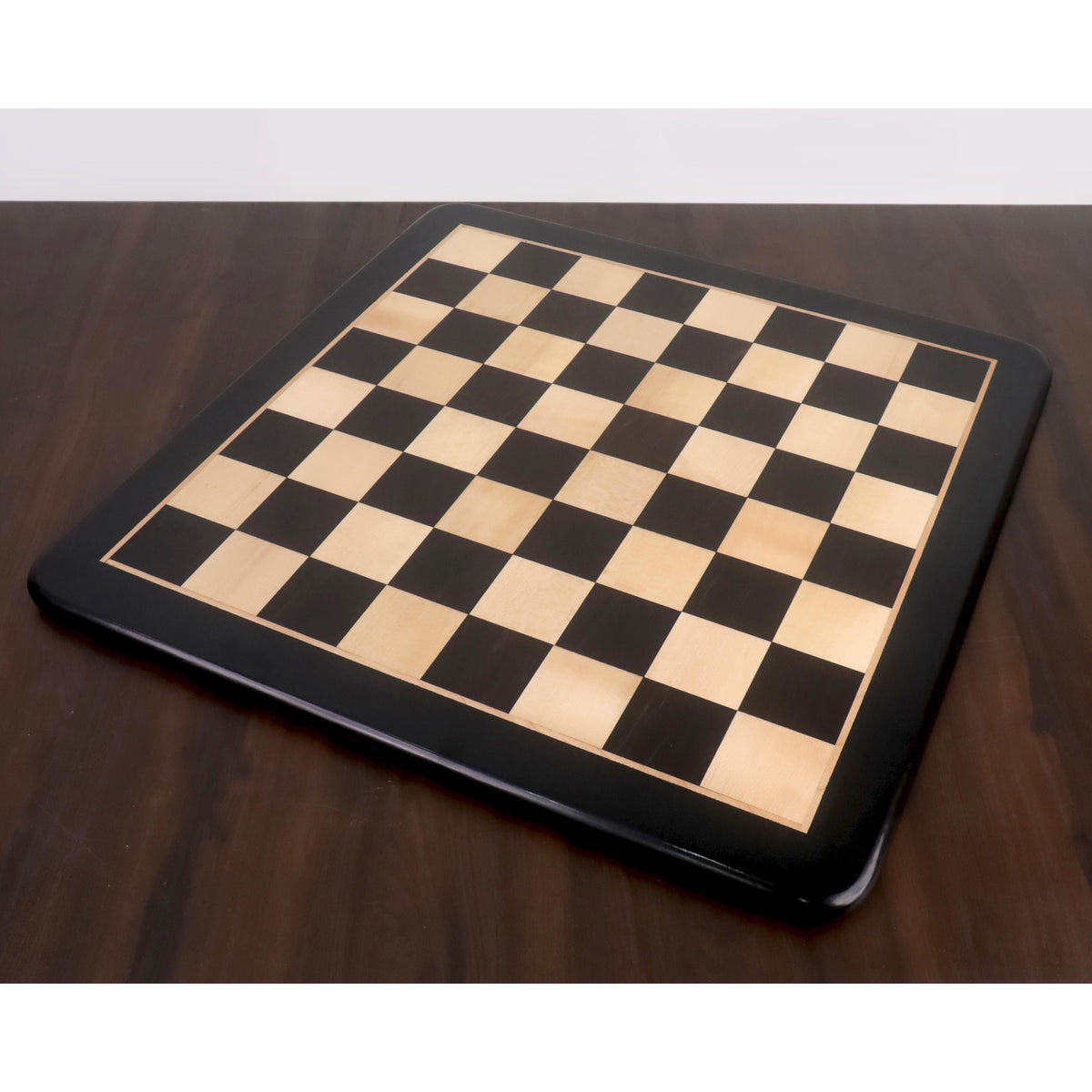 Top perspective view of a 23 inch large inlaid chess board made from genuine ebony and maple wood on a dark wooden table.