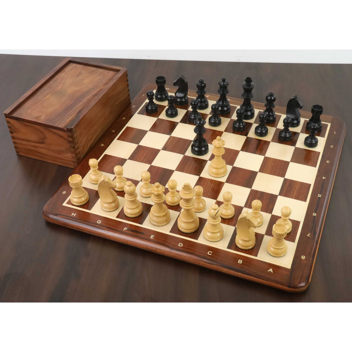Full championship ebonised boxwood chess set arranged on a wooden board next to a wooden storage box.