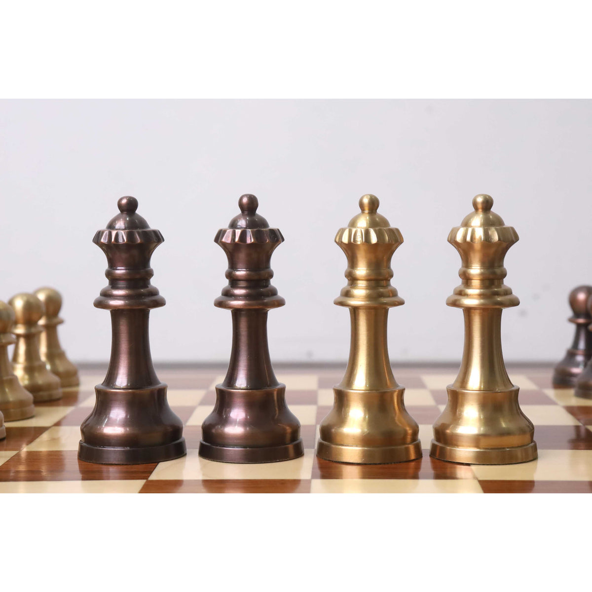 Four Pro Staunton metal chess queens in copper and antique brass finishes standing in a row.