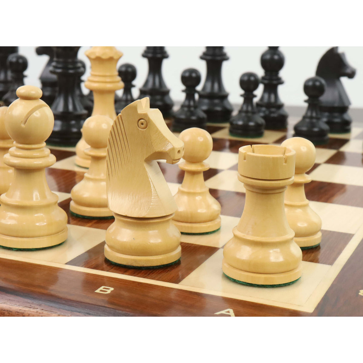 Close-up of a natural boxwood knight and rook on a wooden board, with black ebonised pieces blurred behind.