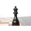 Sharp close-up of a dark ebonised boxwood queen piece standing prominently on the edge of a wooden board.