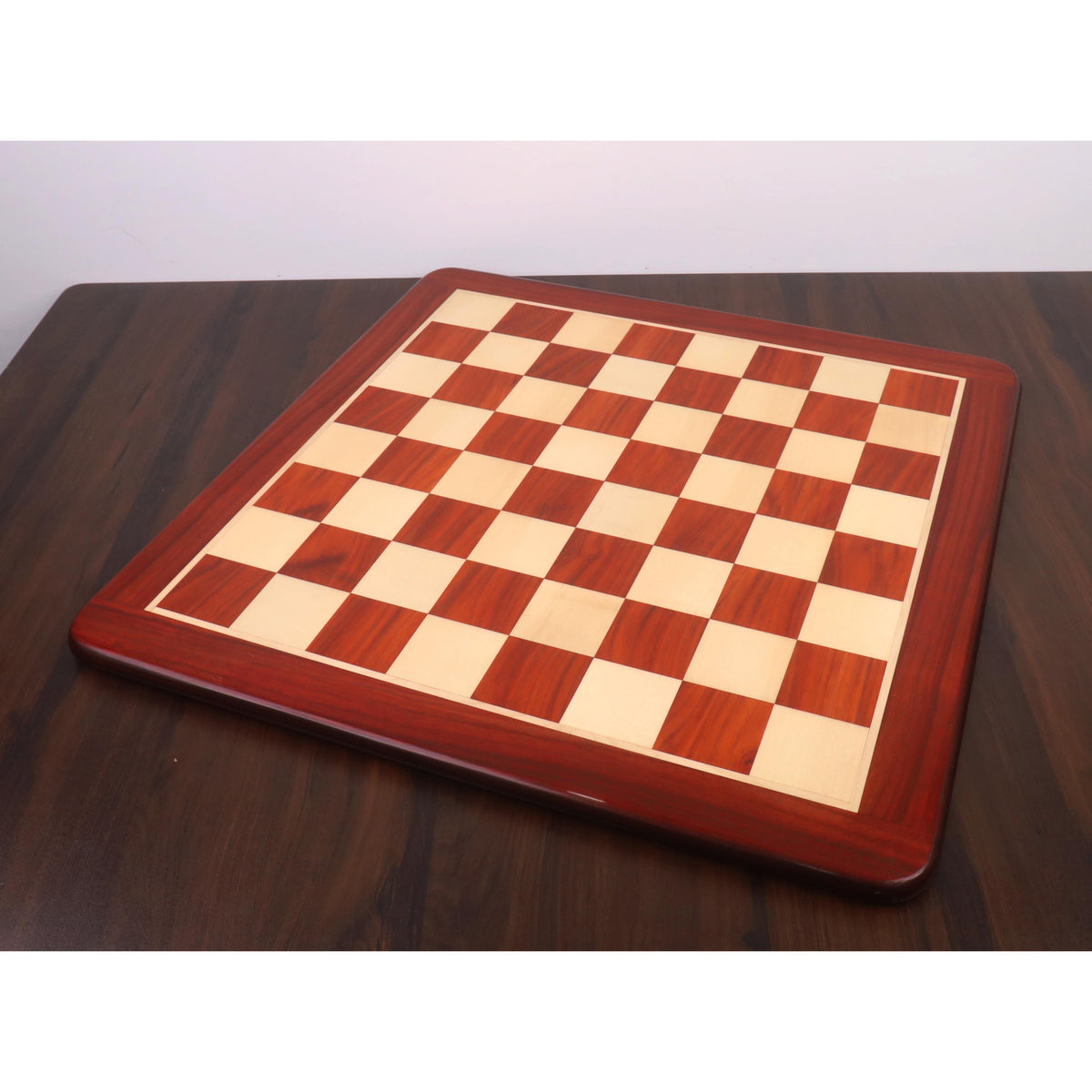Full perspective view of a 25 inch professional wooden chess board with 65mm squares on a dark wood table.