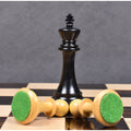 Ebony King chess piece standing over boxwood pieces with green felt bases on a chessboard.