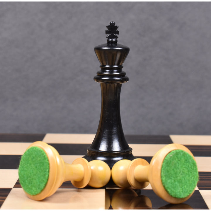Ebony King chess piece standing over boxwood pieces with green felt bases on a chessboard.