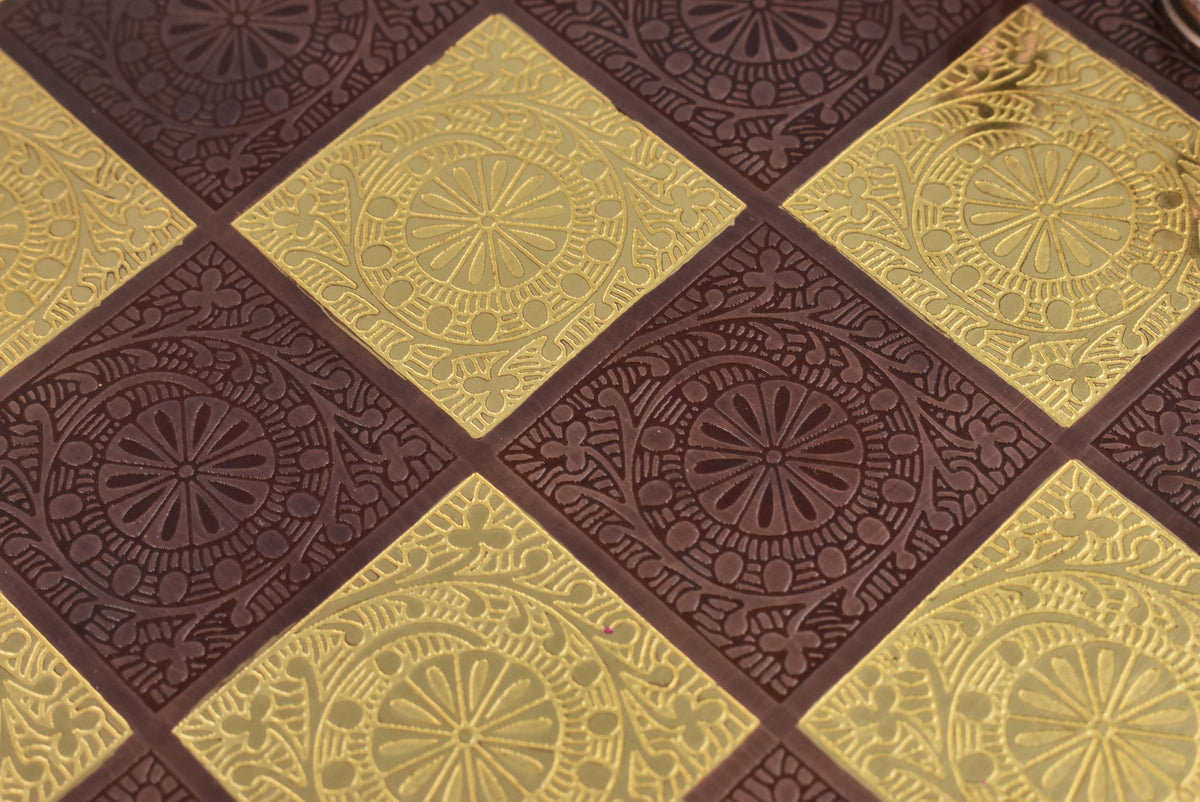 Close-up, overhead view of the detailed floral and geometric embossing on the metal chess board squares.