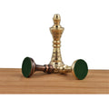 Three Staunton-inspired brass kings lie and stand on a wooden surface, showcasing their green felt bottoms and unique metal finish.