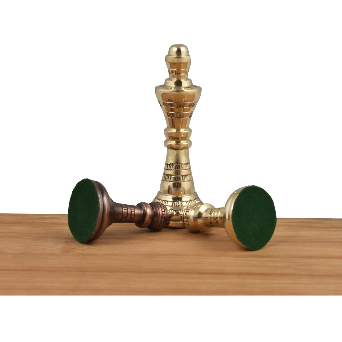 Three Staunton-inspired brass kings lie and stand on a wooden surface, showcasing their green felt bottoms and unique metal finish.