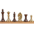 A lineup of the gold brass chess pieces (king, queen, bishop, knight, rook, pawn) on a wooden display.
