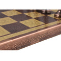 Close-up of the ornate, embossed floral pattern on the edge of the copper and gold metal chess board.