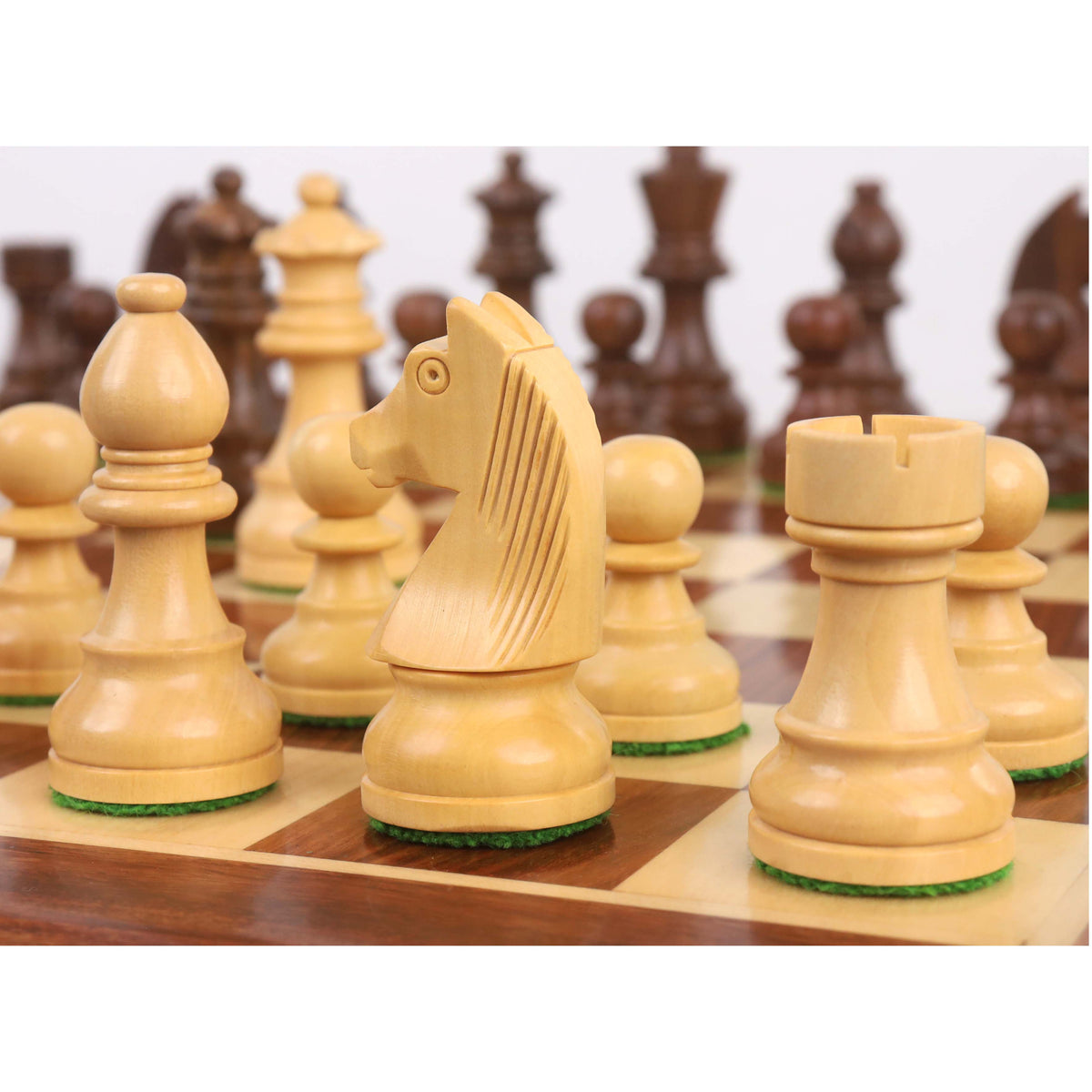 A detailed close-up of the Boxwood Staunton chess knight, with other pieces and the wooden board blurred in the background.