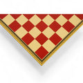 Corner view of a red and beige wooden chessboard with decorative borders.