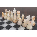 Detailed view of handcrafted white onyx chess pieces on a natural stone board.