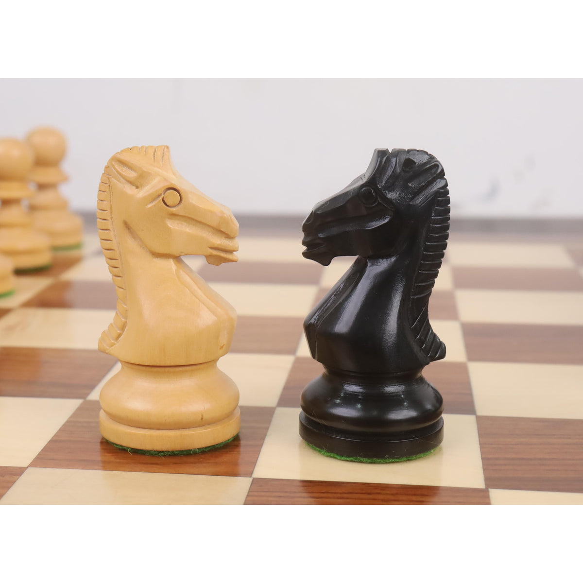 Close-up of light boxwood and dark ebonised knights from the Taj Mahal chess set facing each other.