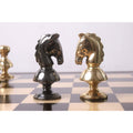 Gold and grey Victorian metal chess knights facing each other on a glossy board.