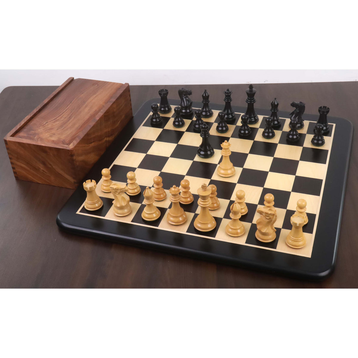 Complete ebony and boxwood chess pieces set arranged on a minimalist black framed wooden chess board with a storage box.