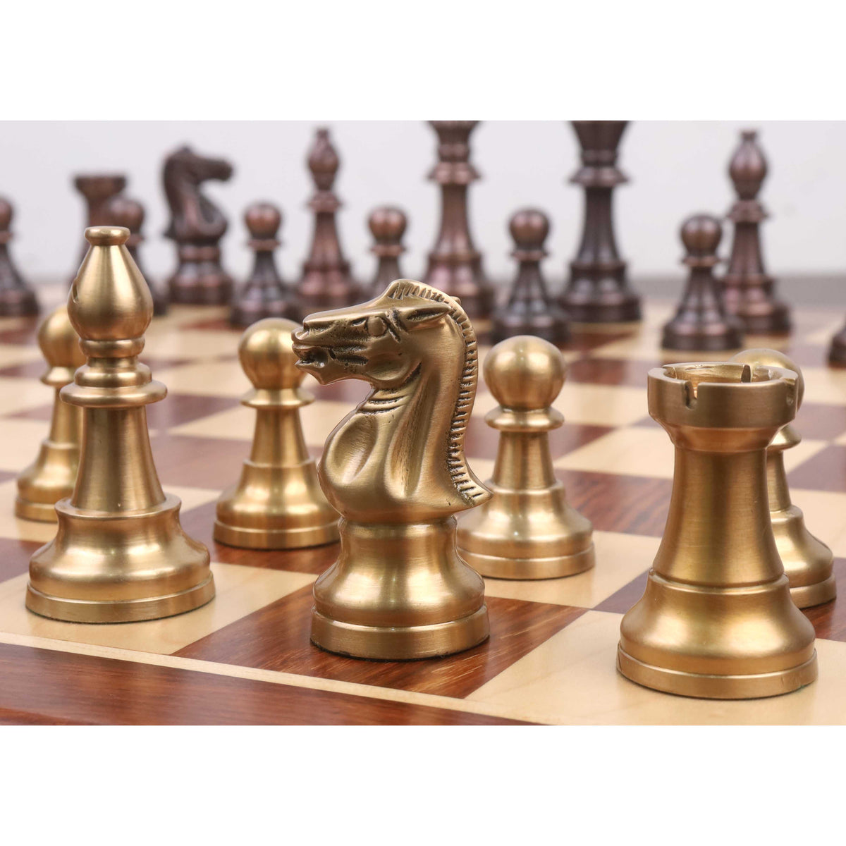 Close-up of an antique brass Pro Staunton knight on a chessboard with other pieces blurred behind.