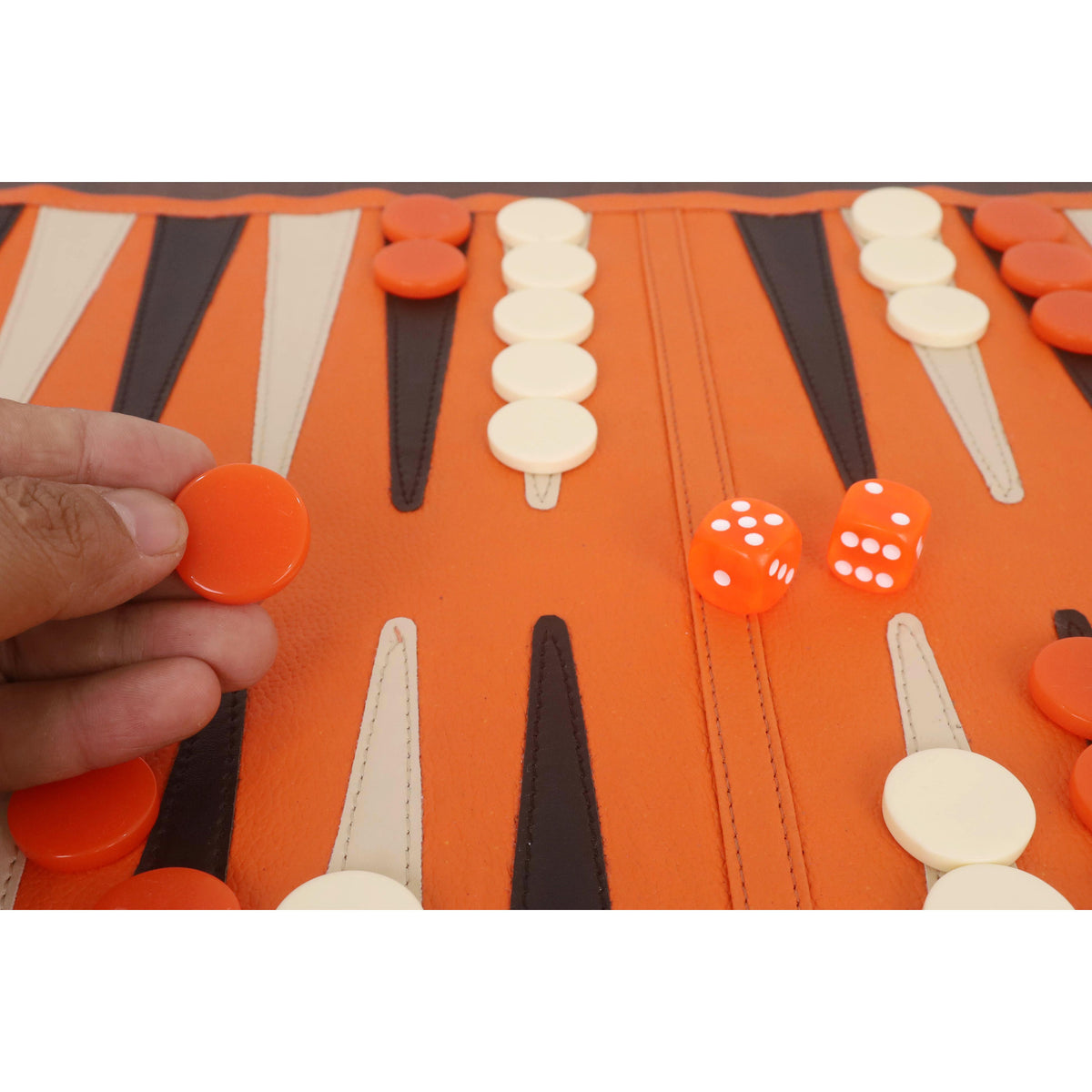 Close-up of a player holding an orange backgammon checker on the game board.