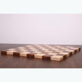 Low-angle view of a golden rosewood and maple end grain chess board lying flat on a table.