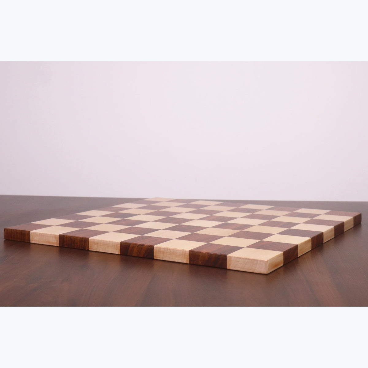 Low-angle view of a golden rosewood and maple end grain chess board lying flat on a table.