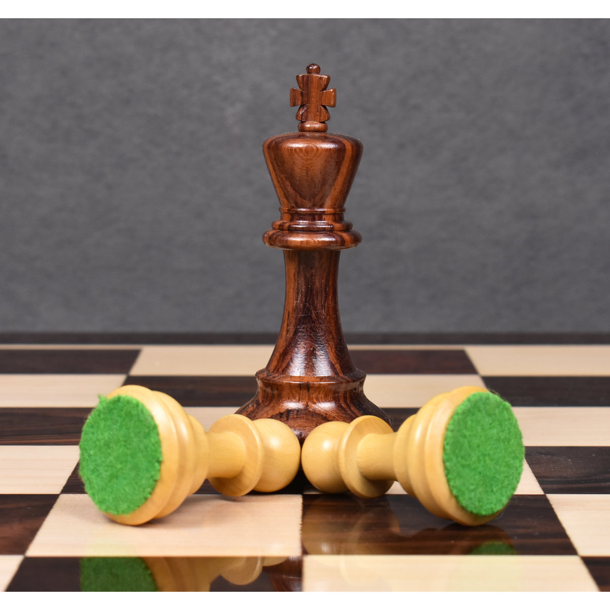 One dark king standing with two light pawns lying on their side on the chessboard.