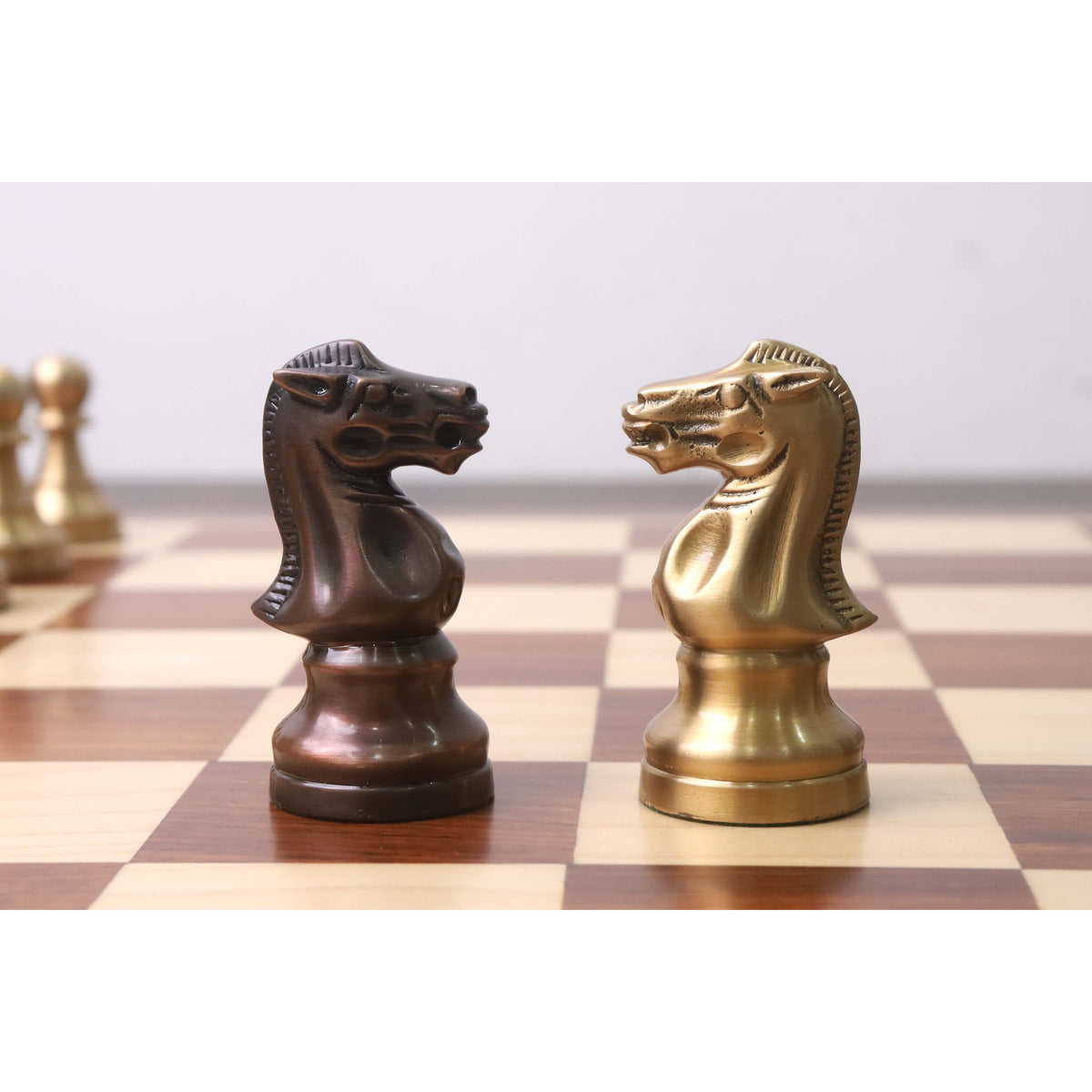 Copper and antique brass Pro Staunton metal chess knights facing each other on a wooden chessboard.