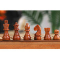 Close-up of intricately carved dark wooden chess pieces on a travel-sized board.