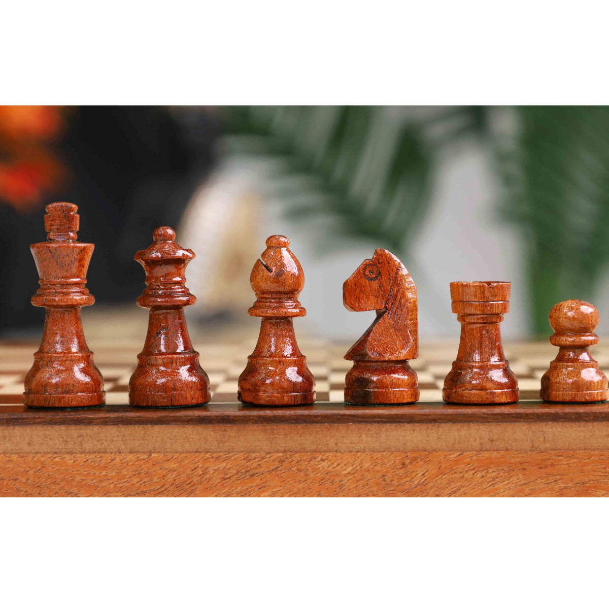 Close-up of intricately carved dark wooden chess pieces on a travel-sized board.