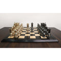 Luxury brass metal chess set showing gold and grey Victorian pieces squared off on a dark bordered board.