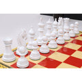 Side-angle perspective of white lacquered boxwood chess pieces lined up on a red and cream chessboard.