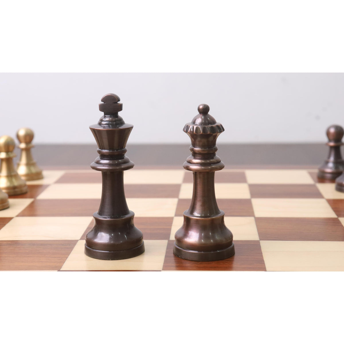 Close-up of a copper metal Pro Staunton king and queen standing together on a chessboard.