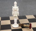 Intricately carved white camel bone owl chess piece standing next to a fallen antiqued piece on a board.