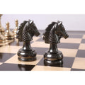 Two metallic grey knights from the Splendor Series brass luxury chess set positioned closely on a wooden chessboard.